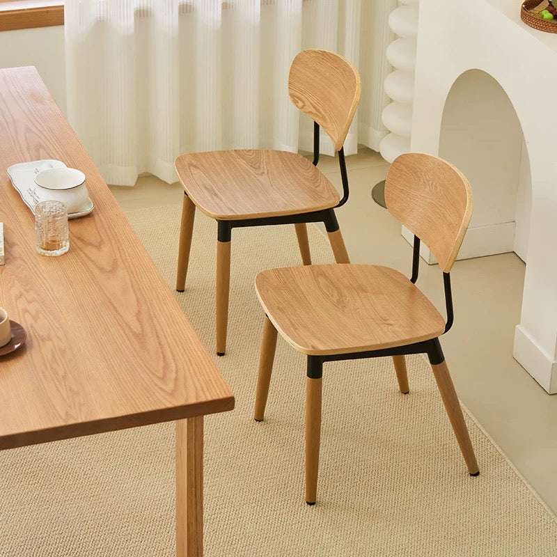 Wooden chairs and table in a room with white curtains and a fireplace.