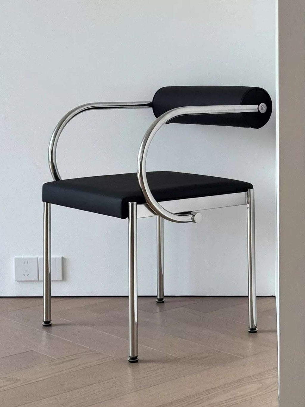 Modern black chair with chrome frame on a wooden floor against a white wall.