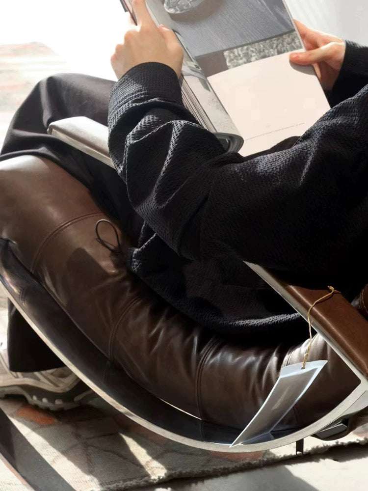 Person sitting in a chair with a book, wearing a black sweater and brown shoes.