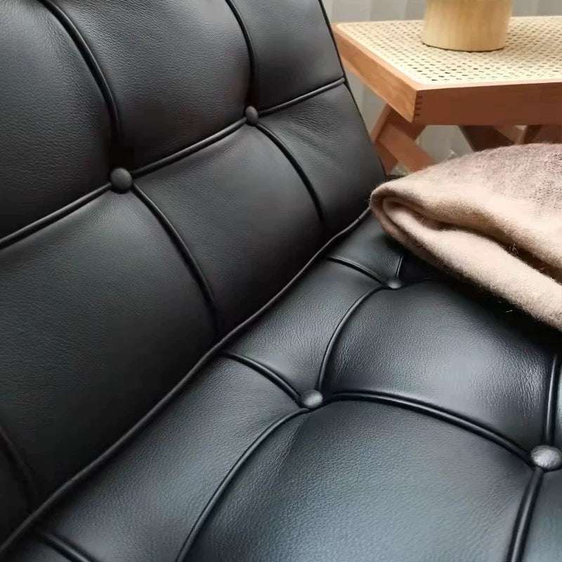 Close-up of a black leather sofa with a wooden side table in the background.