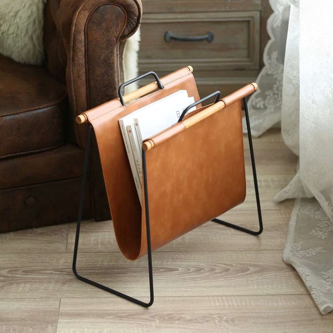 Brown leather magazine rack on a wooden floor next to a brown sofa.