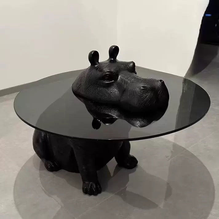 Black hippo-shaped coffee table with glass top on a light gray floor.