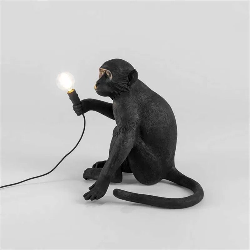 Black monkey lamp holding a light bulb on a white background