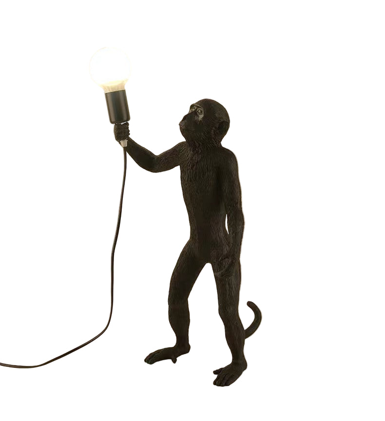 Black monkey-shaped lamp holding a light bulb against a beige background