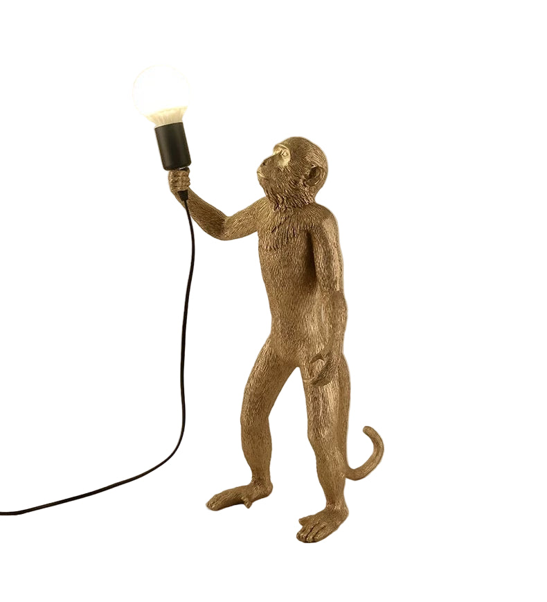 Gold monkey lamp holding a light bulb against a beige background