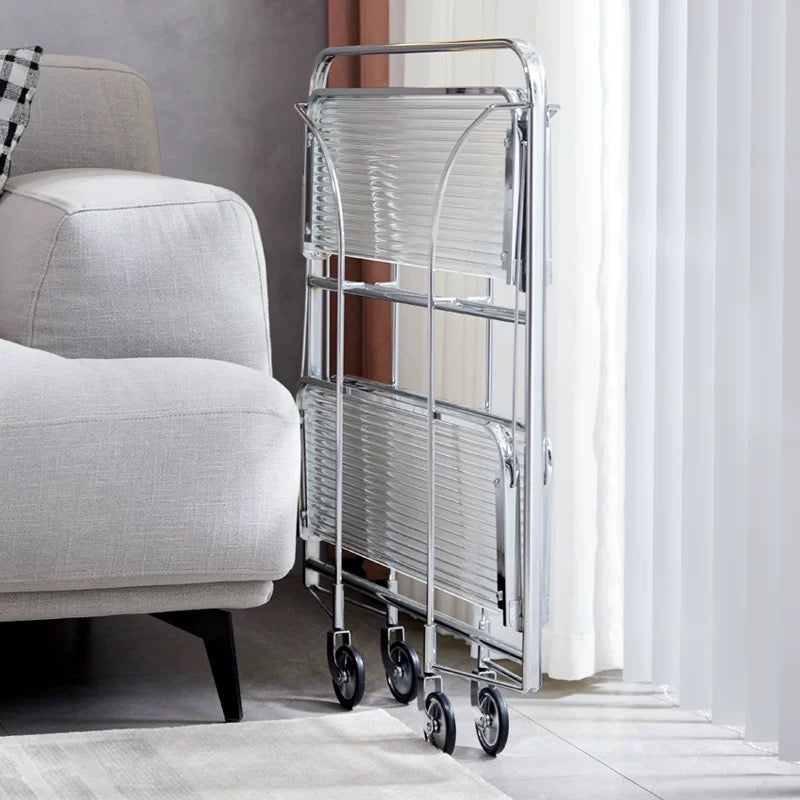 Metal rolling cart with glass shelves next to a gray armchair in a room with white curtains.