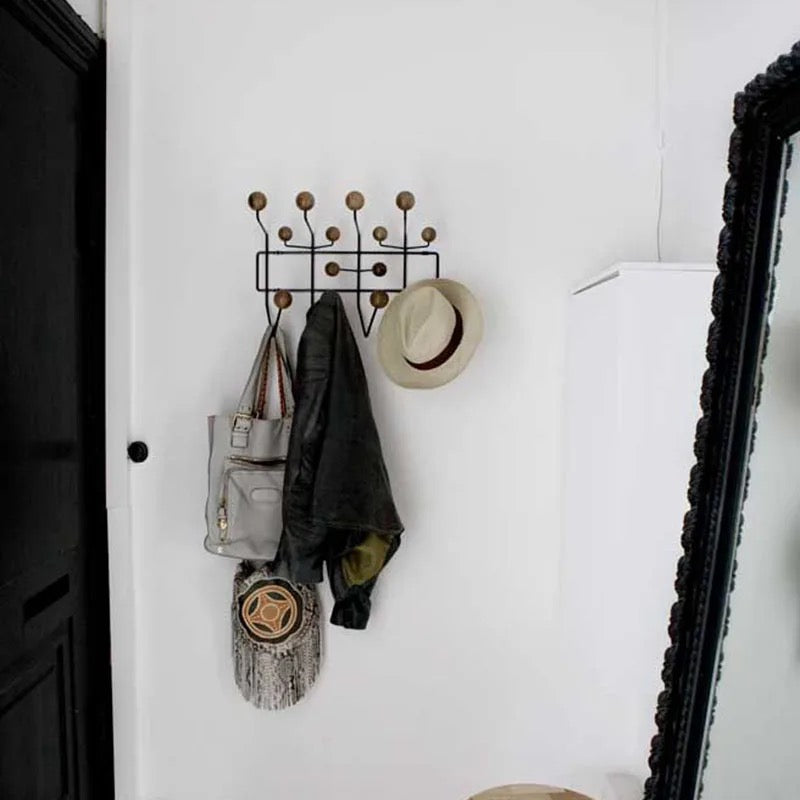 Wall-mounted coat rack with bags, coats, and a hat on a white wall.