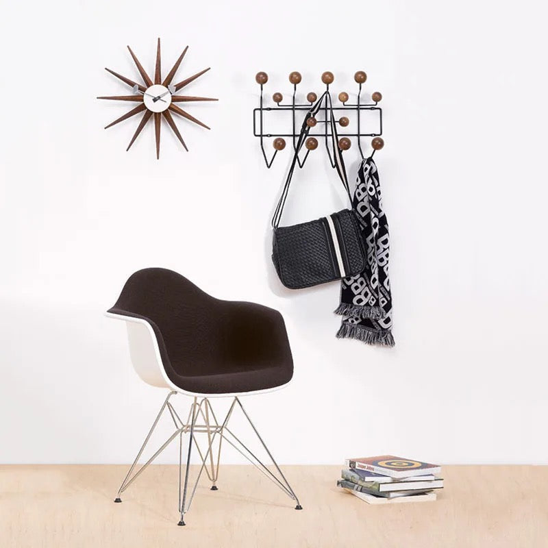 Modern chair next to a wall-mounted coat rack with a bag and scarf, against a white wall.