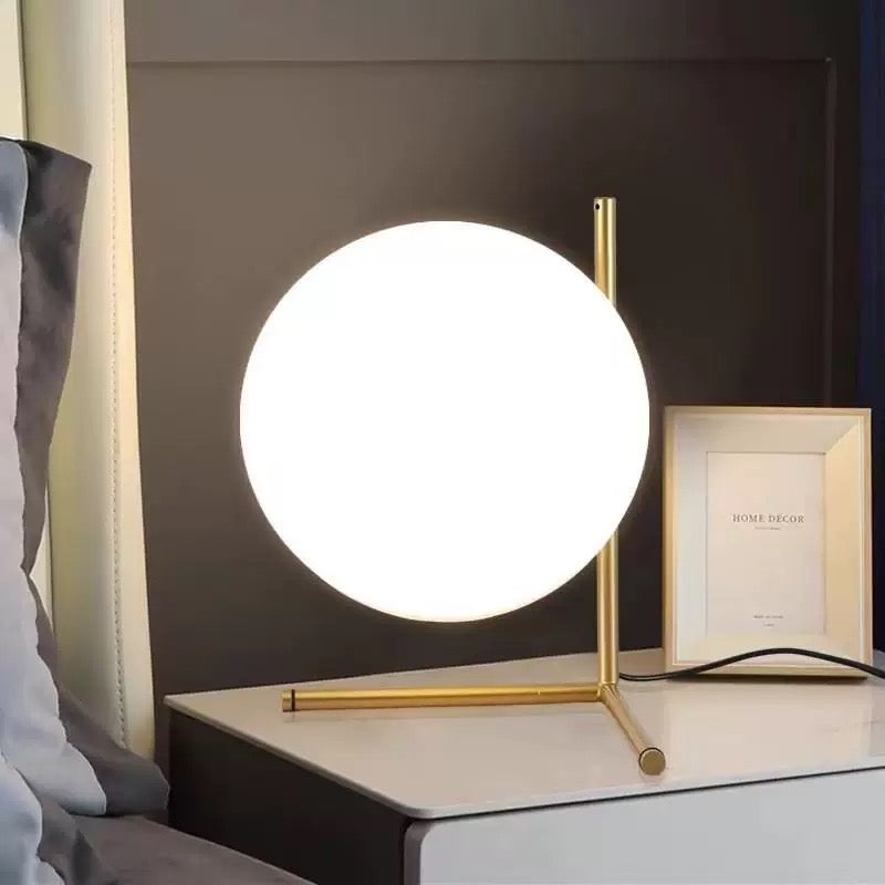 Modern table lamp with a round white shade on a nightstand next to a framed picture.
