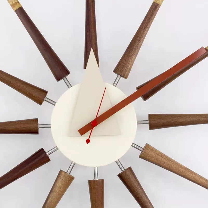 Modern wall clock with wooden spokes and a white face on a white background