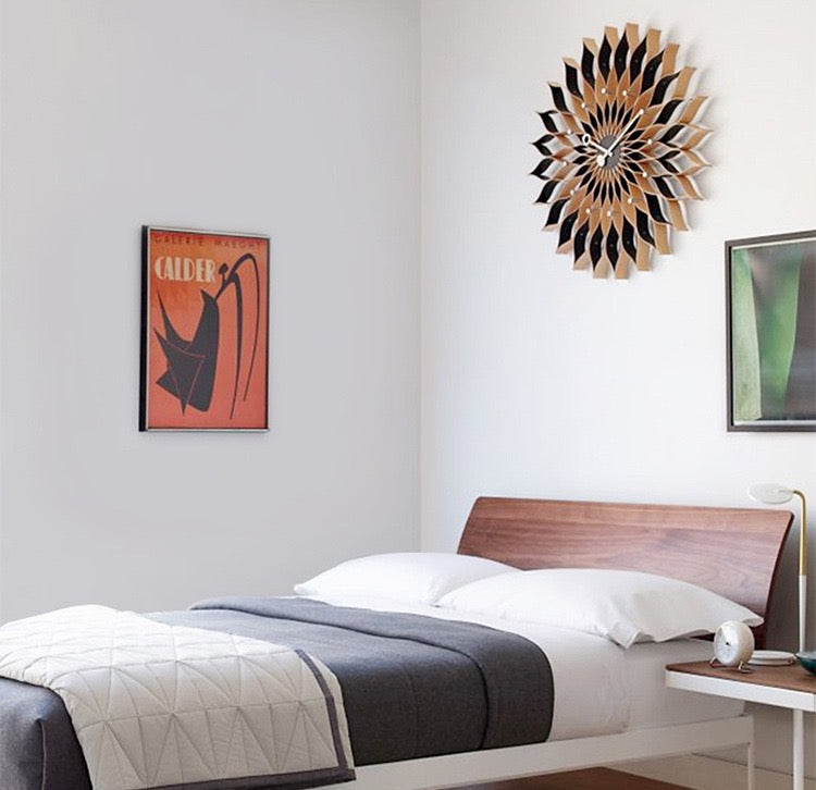 Modern bedroom with wooden bed, wall clock, and artwork on a white wall.