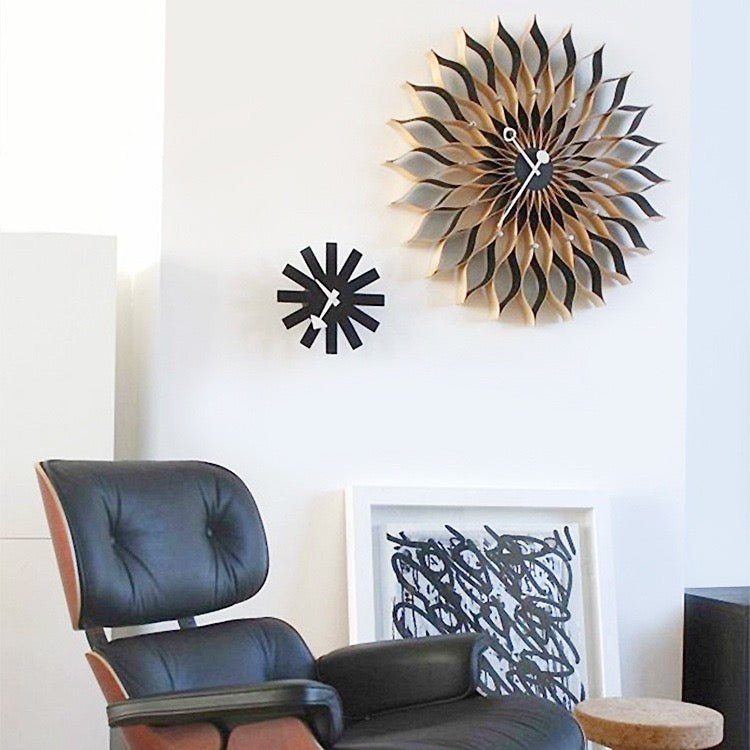 Modern black chair in a room with decorative wall clocks and abstract art.