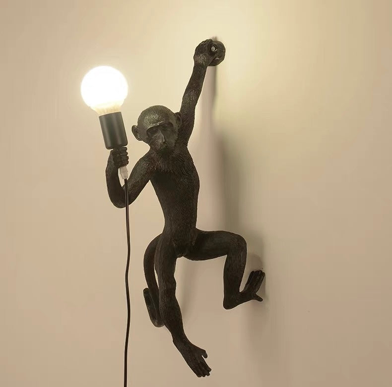Black monkey wall lamp holding a light bulb against a beige background