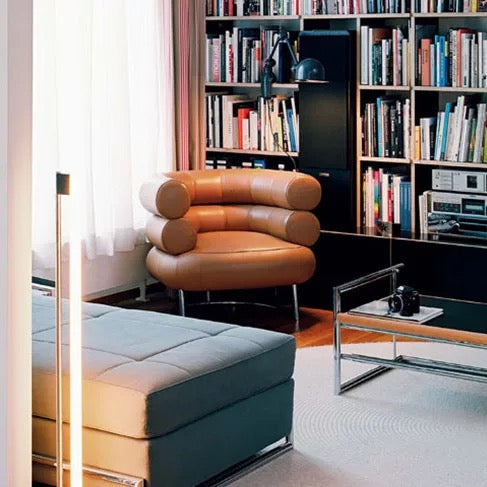 Modern living room with a brown armchair, ottoman, and bookshelf filled with books.