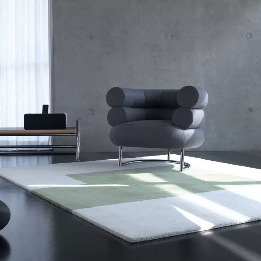 Modern gray armchair on a green and white checkered rug in a minimalistic room.