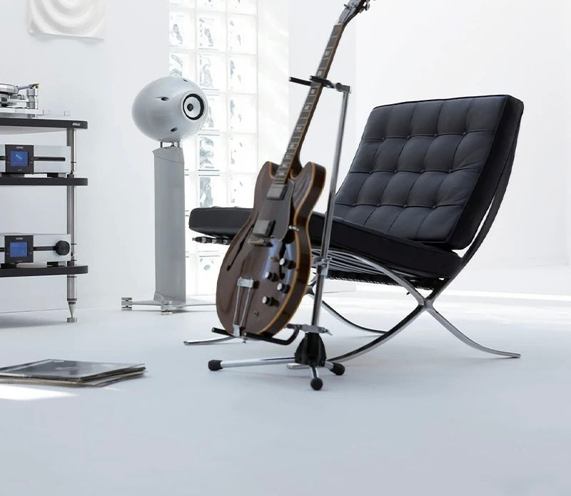 Modern black chair with a guitar on a stand in a minimalistic room.