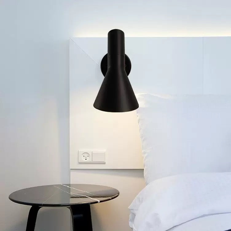 Black wall lamp on a white wall above a bed with a side table.