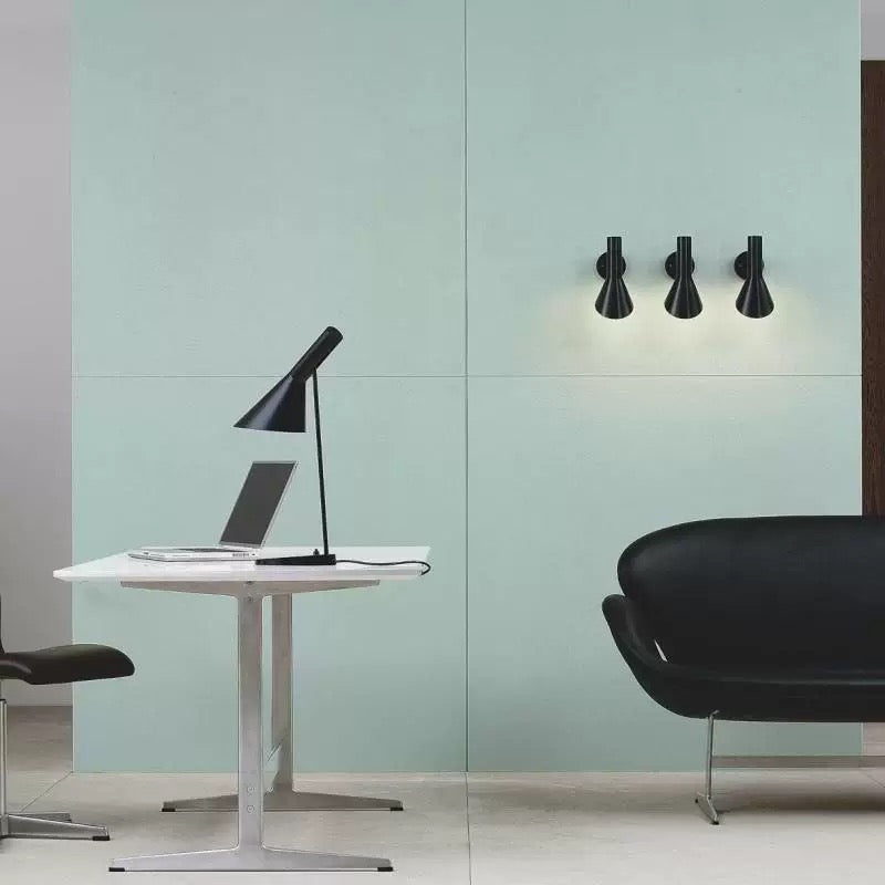 Modern office setup with a desk, chair, and wall-mounted lamp against a light green wall.