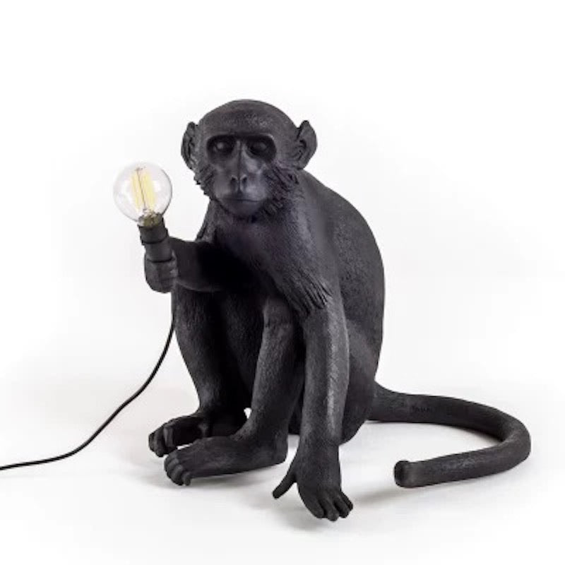 Black monkey lamp holding a light bulb on a white background