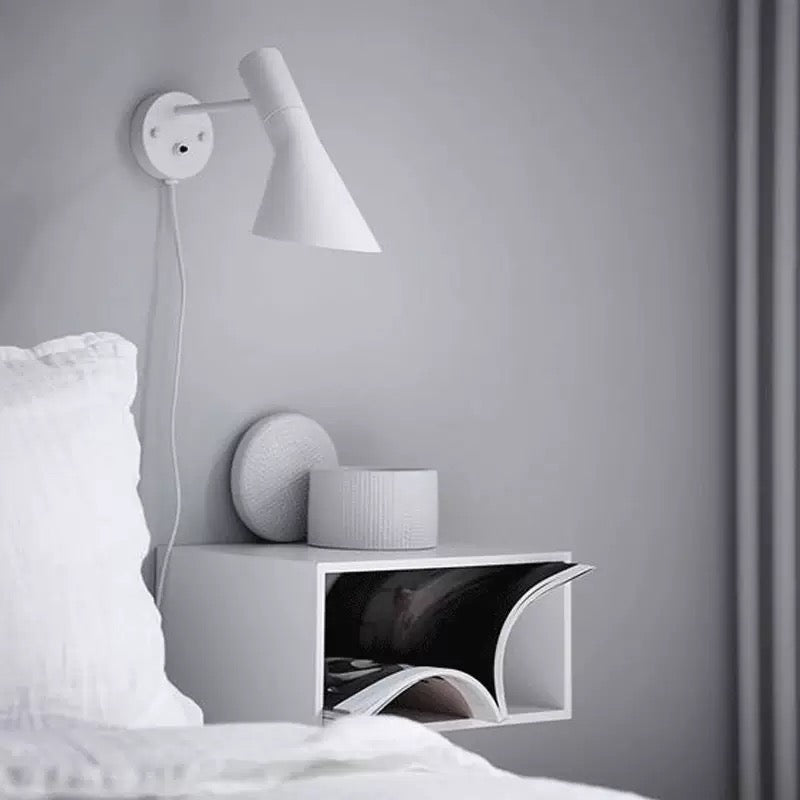 Modern wall lamp on a gray wall above a nightstand with a magazine.