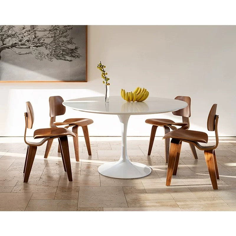 Dining room with a white round table and wooden chairs, featuring a vase and bananas on the table.