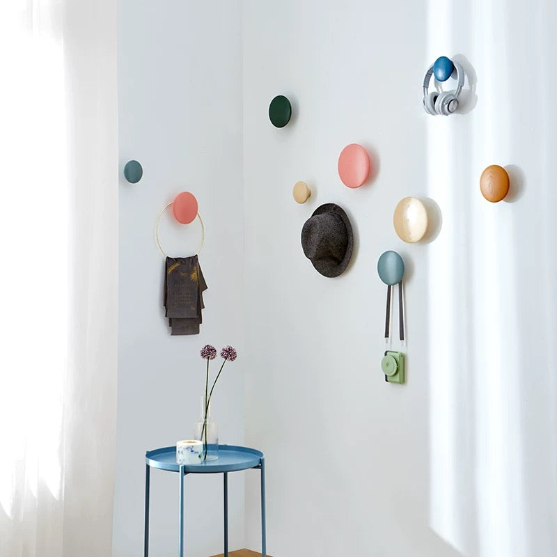 Colorful wall hooks on a white wall with a small table and flowers.