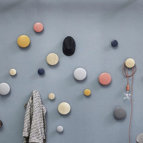 Colorful round wall hooks on a gray wall with a coat and light bulb.