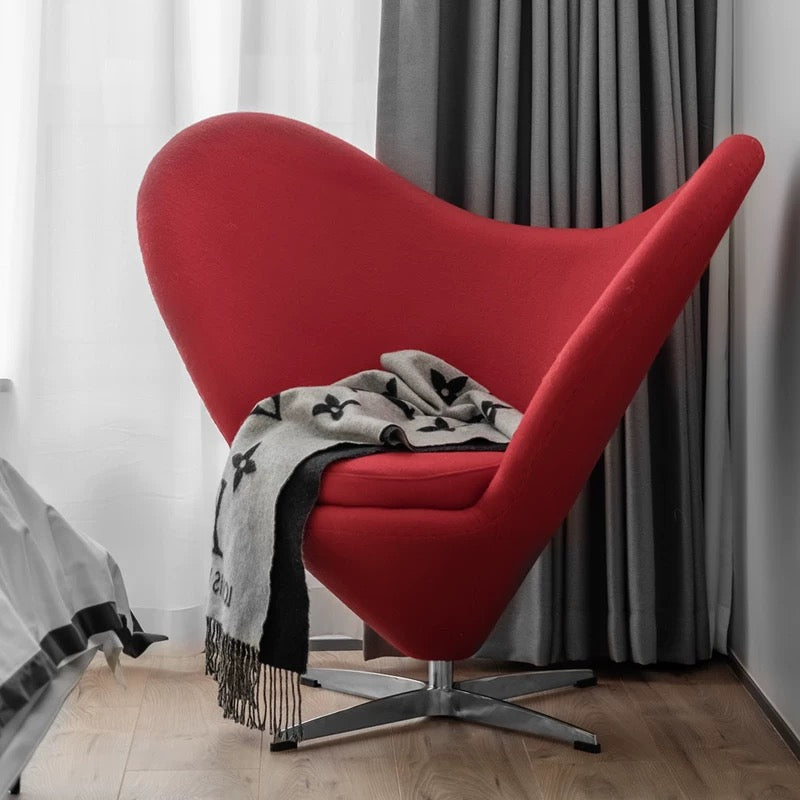 Red heart-shaped chair with a gray blanket against a neutral background