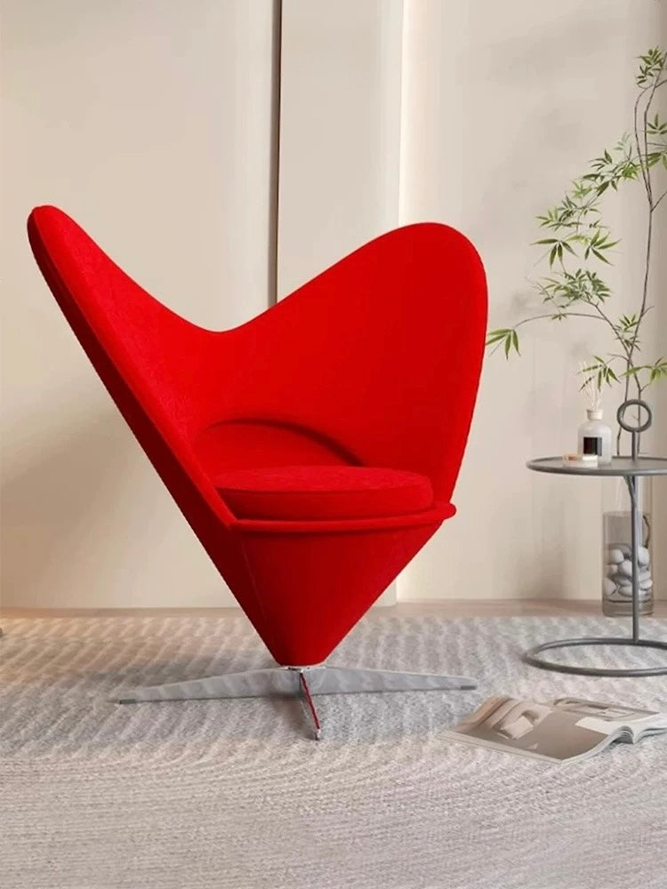 Red heart-shaped chair in a modern room with a plant and table.
