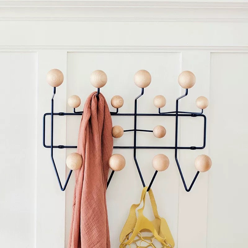 Wall-mounted coat rack with wooden knobs holding a pink scarf and yellow coat against a white wall.