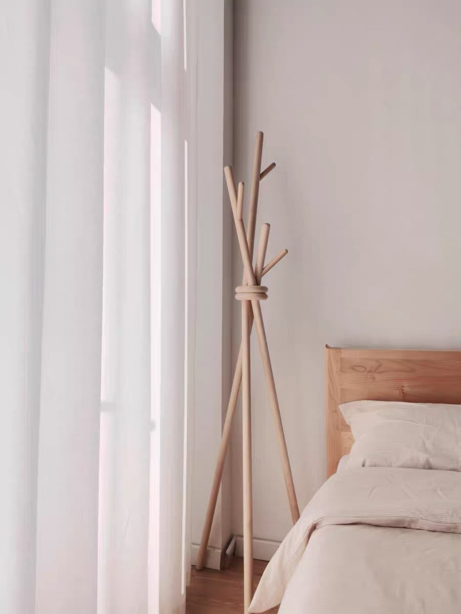 Wooden coat rack against a wall in a bedroom with a bed and curtains.