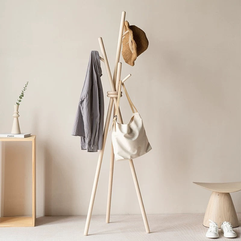 Wooden coat rack with clothes and a bag against a beige wall.
